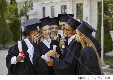 Happy graduate people i ngraduation clothes looking at diploma after ceremony in campus. Happy graduate people i ngraduation clothes looking at diploma after ceremony in campus. 129670596