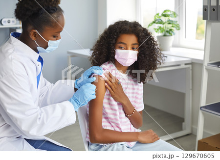 An African-American woman doctor treats the girl's shoulder area before vaccination. An African-American woman doctor treats the girl's shoulder area before vaccination. 129670605