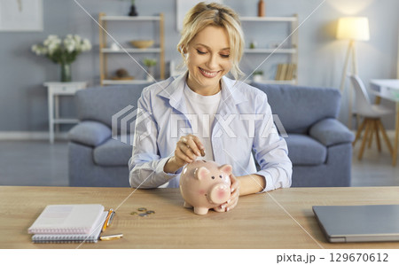 Happy woman putting coin in piggybank to enjoy saving money, managing household budget at home 129670612
