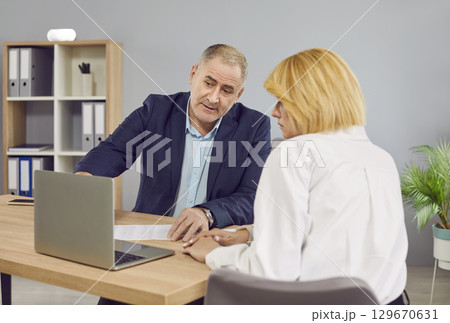 Two business people work in office. Two employers sitting with laptop computer and talking. 129670631