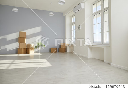 Unpacked cardboard boxes are stacked on the floor in the empty room in new apartment. 129670648
