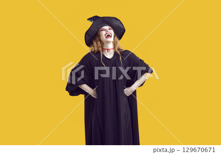 Funny woman in witch Halloween costume holding hands on hips and laughing loudly 129670671