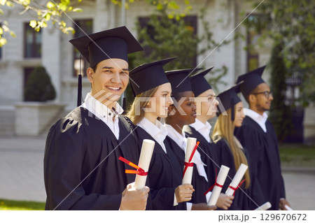 Happy graduate students dressed in black graduation gowns holding diplomas Happy graduate students dressed in black graduation gowns holding diplomas 129670672