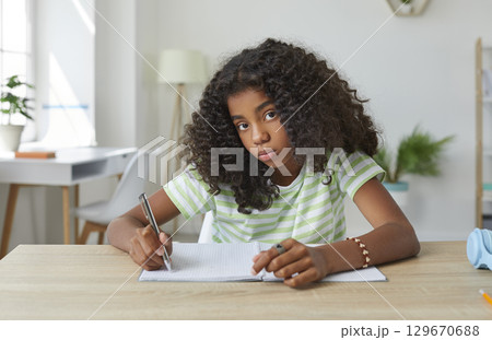Portrait of an African American school girl while doing homework at her desk at home Portrait of an African American school girl while doing homework at her desk at home 129670688