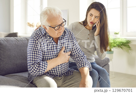 Worried woman calling emergency ambulance to senior father suffering from heart attack at home. 129670701