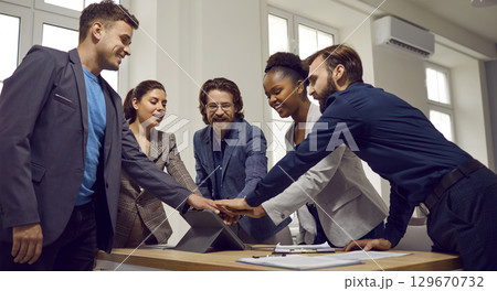 Multiracial team of happy young business people stacking hands after work meeting 129670732
