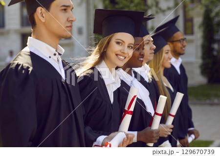 Group of multicultural people in graduation gowns and caps graduate universuty standing in line. Group of multicultural people in graduation gowns and caps graduate universuty standing in line. 129670739