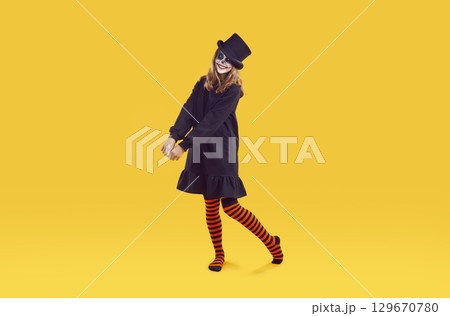 Happy teen girl with Halloween skull makeup posing over isolated yellow background Happy teen girl with Halloween skull makeup posing over isolated yellow background 129670780