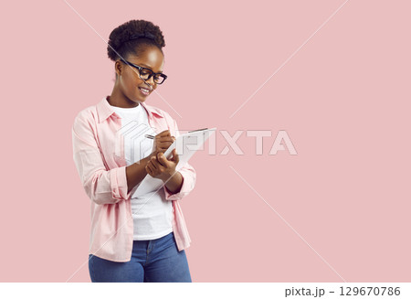 Smiling young African American woman writing down notes in clipboard 129670786