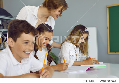 Young happy teacher is engaged with students, standing next to student and holding her shoulder approvingly. Young happy teacher is engaged with students, standing next to student and holding her shoulder approvingly. 129670788