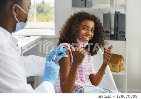 Happy teenage girl showing thumbs up gesture while being immunized against viral infections. 129670809