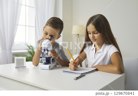 Two little school children take notes while looking at something under microscope Two little school children take notes while looking at something under microscope 129670841