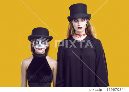 Serious mother and daughter in Halloween outfits looking at you waiting for trick or treat. 129670844