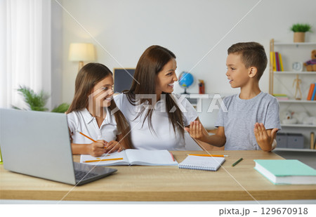 Caring and friendly young mother helps her children to complete their school homework. 129670918