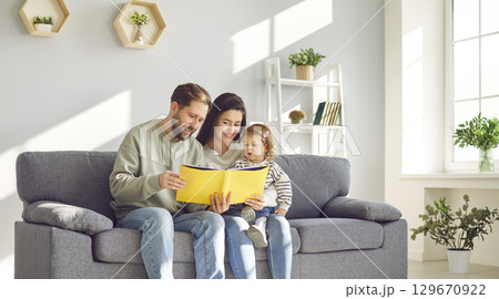 Happy mom and dad reading book to their little daughter 129670922