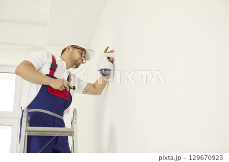 Worker installing a surveillance CCTV dome camera on the wall inside the building 129670923