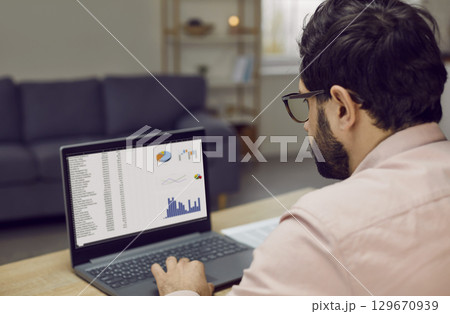 Focused businessman working with analytics using laptop sitting at workplace 129670939
