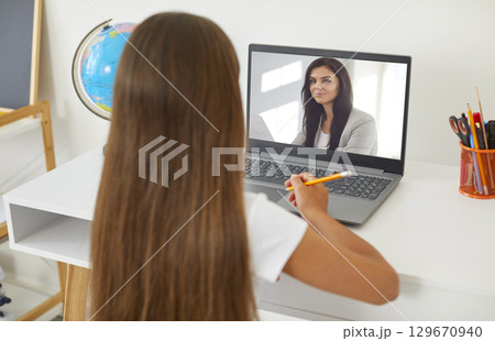 Young female teacher having video conference call with a child girl pupil using webcam. 129670940
