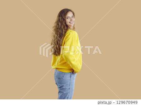 Happy girl in yellow sweatshirt and blue jeans posing isolated on beige background Happy girl in yellow sweatshirt and blue jeans posing isolated on beige background 129670949