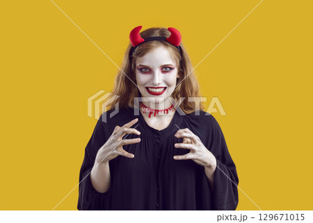 Woman trying to catch somebody in halloween costume with terrifying makeup on yellow background. 129671015