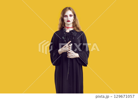 Portrait of woman with bloody creepy makeup holding black rose in her hands and looking at camera. Portrait of woman with bloody creepy makeup holding black rose in her hands and looking at camera. 129671057