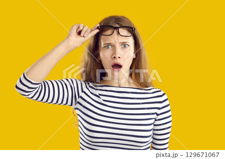 Young woman looking at something with a funny, confused, shocked face expression 129671067