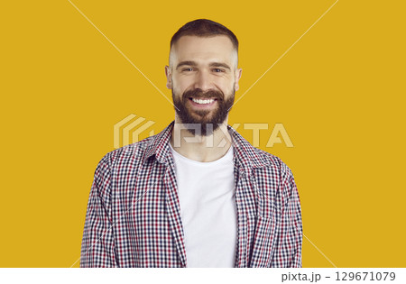 Portrait of happy smiling brunet man in red plaid shirt on yellow background looking at camera. 129671079