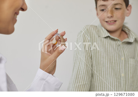 Audiologist gives a modern hearing aid to a child patient with some hearing loss Audiologist gives a modern hearing aid to a child patient with some hearing loss 129671080