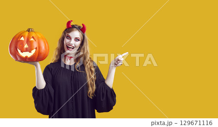 Happy woman in Halloween costume advertising Halloween party on yellow copy space background Happy woman in Halloween costume advertising Halloween party on yellow copy space background 129671116