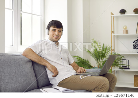 Cheerful male student freelancer at home watching online training or webinar on laptop. 129671146