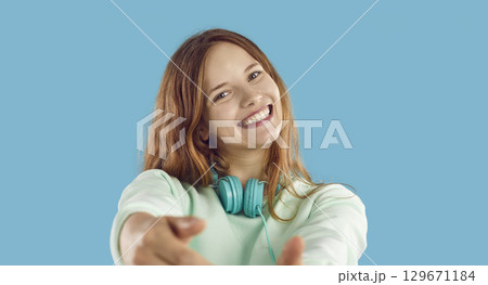 Happy girl with headphones looking at camera and smiling on blue studio background 129671184