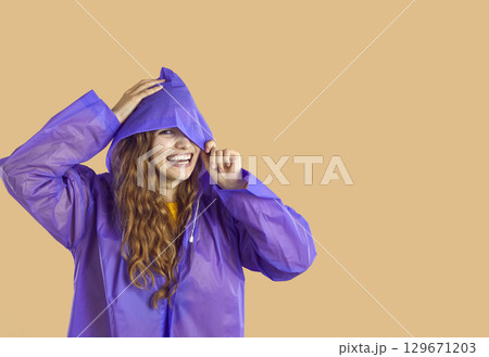 Happy young woman in purple raincoat standing isolated on beige copy space background Happy young woman in purple raincoat standing isolated on beige copy space background 129671203