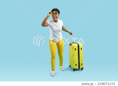 African american woman with big yellow suitcase isolated on blue wall. African american woman with big yellow suitcase isolated on blue wall. 129671215