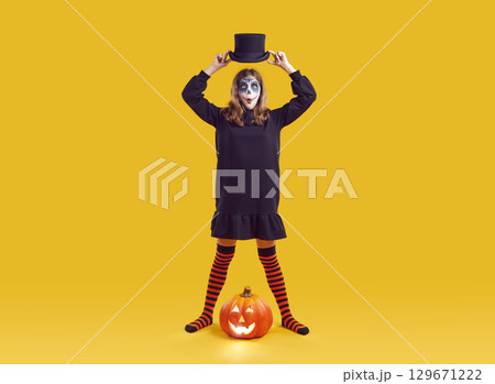 Portrait of funny teenage girl with Halloween makeup looking surprised on orange background. Portrait of funny teenage girl with Halloween makeup looking surprised on orange background. 129671222