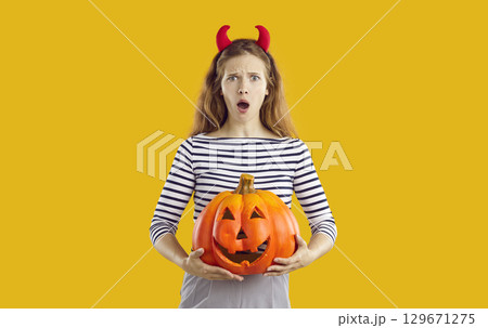 Beautiful young woman with funny surprised face expression holding Halloween pumpkin 129671275