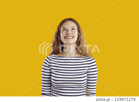 Young cheerful long haired Caucasian woman millennial in striped clothes smiling broadly looks up 129671279