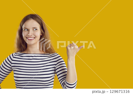 Happy beautiful young woman pointing to copy space side on yellow color background Happy beautiful young woman pointing to copy space side on yellow color background 129671316