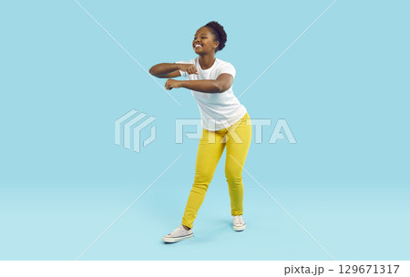 Young African American woman performs funny dance enjoying life standing in turquoise studio Young African American woman performs funny dance enjoying life standing in turquoise studio 129671317