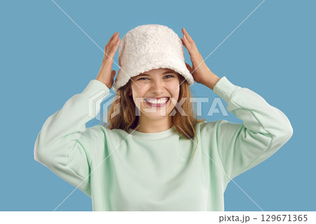 Portrait of laughing girl in white warm fluffy hat and mint sweatshirt on light blue background. Portrait of laughing girl in white warm fluffy hat and mint sweatshirt on light blue background. 129671365
