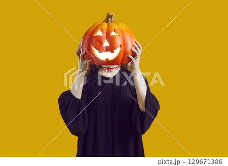 Unrecognizable woman with bloody cut on her neck hides her face behind glowing Halloween pumpkin. 129671386