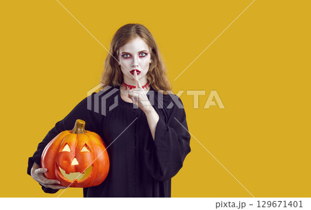 Attractive woman in halloween clown make-up holding curved pumpkin with keep quite gesture. 129671401