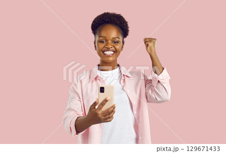 Overjoyed African American woman makes YES gesture with hand when sees notification on mobile phone 129671433