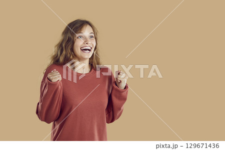 Happy excited amazed woman with yes win gesture in red sweatshirt in beige background. Happy excited amazed woman with yes win gesture in red sweatshirt in beige background. 129671436