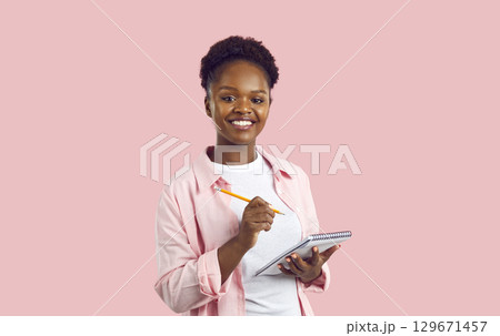 Happy beautiful young African American woman holding a pencil and writing in her notebook Happy beautiful young African American woman holding a pencil and writing in her notebook 129671457