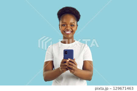 Happy smiling afroamerican woman with smartphone is looking at camera on turquoise background. 129671463