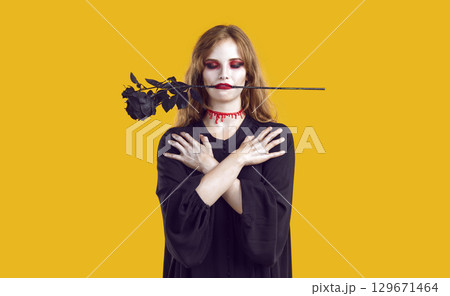 Young woman in spooky Halloween costume, with blood on neck and black rose in mouth 129671464