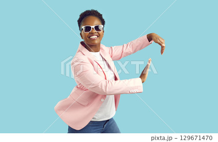 Happy African American woman in a trendy outfit dancing isolated on a blue background Happy African American woman in a trendy outfit dancing isolated on a blue background 129671470