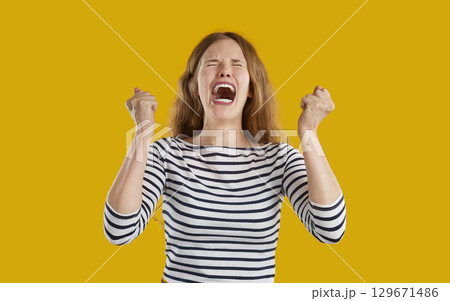 Funny young woman feeling very angry and frustrated, clenching fists and screaming Funny young woman feeling very angry and frustrated, clenching fists and screaming 129671486