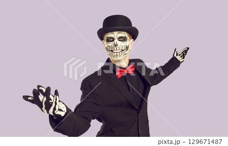 Happy man with skeleton make-up posing at Halloween costume party on light lilac background. Happy man with skeleton make-up posing at Halloween costume party on light lilac background. 129671487