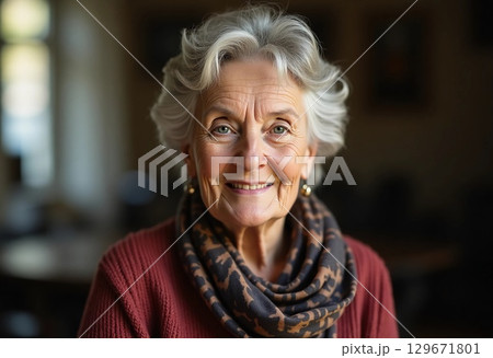A delightful older woman with silver hair and a warm smile radiates happiness while wearing a patterned scarf. The soft indoor light creates a welcoming atmosphere Generative AI 129671801